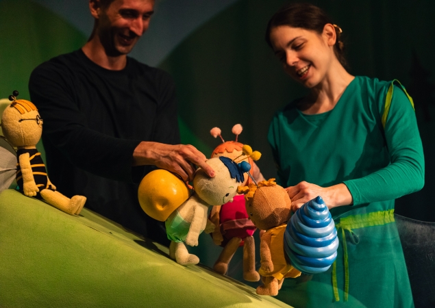 Bogyó és Babóca – két bábjátékos nevetve mozgatja a bábokat a zöld domboldalon